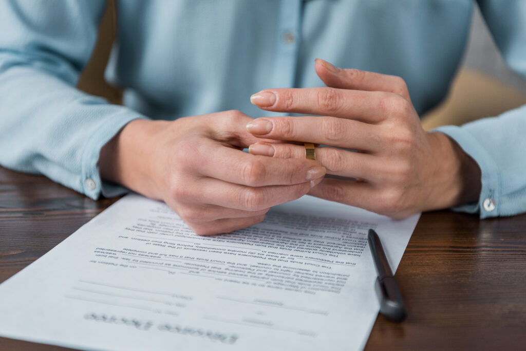 cropped shot of woman taking off wedding ring and divorce decree on table